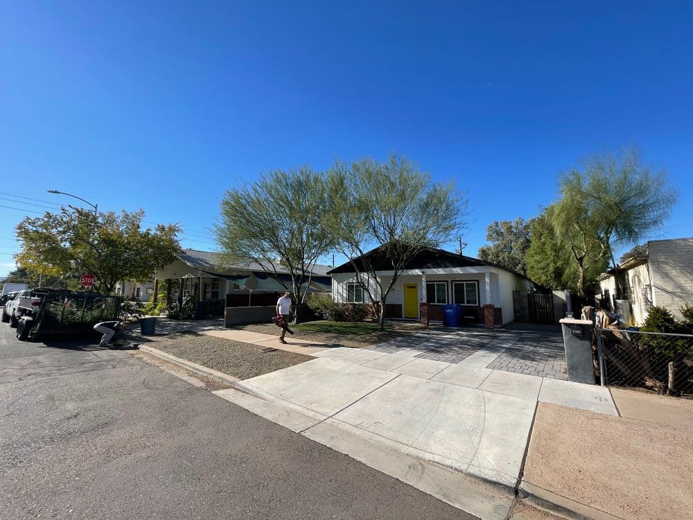 Residential street view with trees, sidewalks, and two houses under clear blue sky.