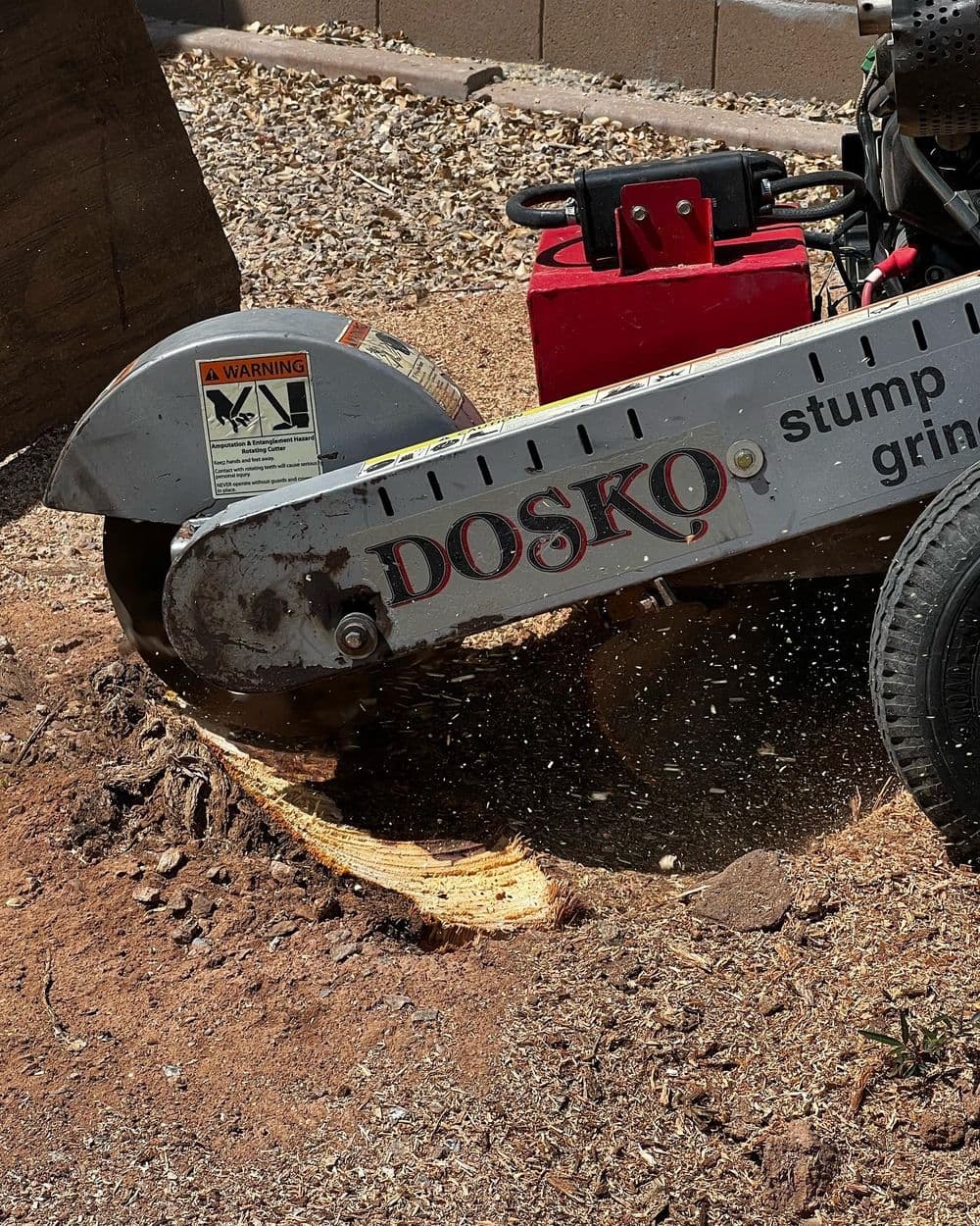 Stump grinder in action, cutting through wood, with safety warning label visible.